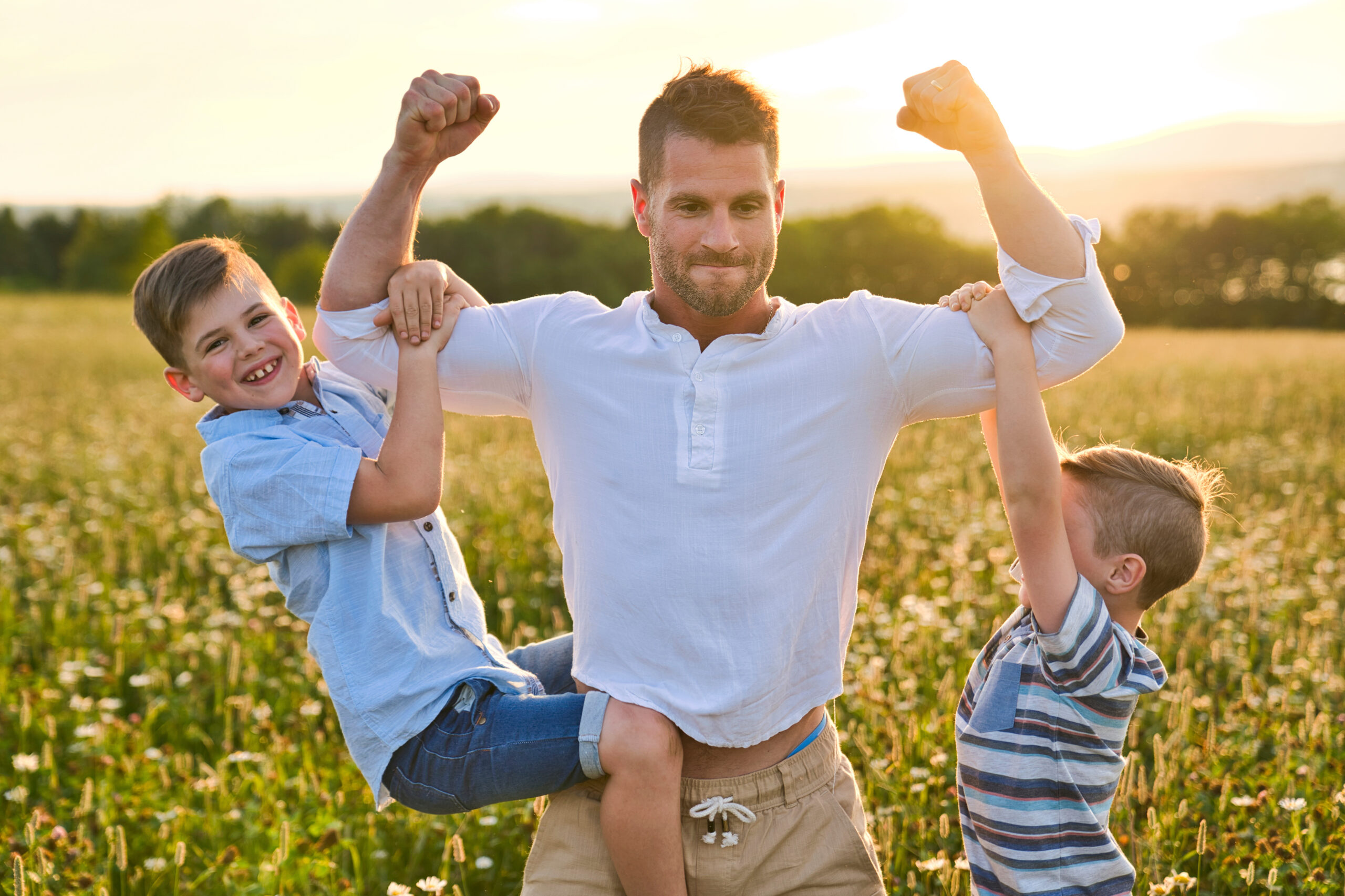 A happy family of father and is two childs on field at the sunset having fun