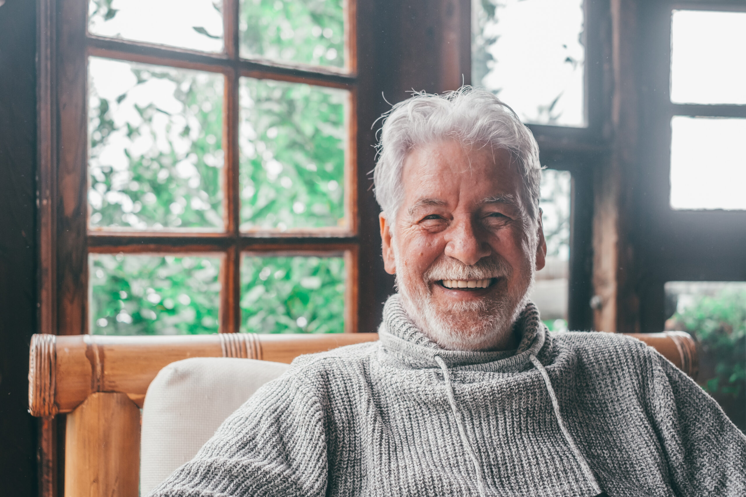 Portrait of old man smiling and looking at the camera sitting on the sofa from home. Closeup male person senior cheerful indoor.