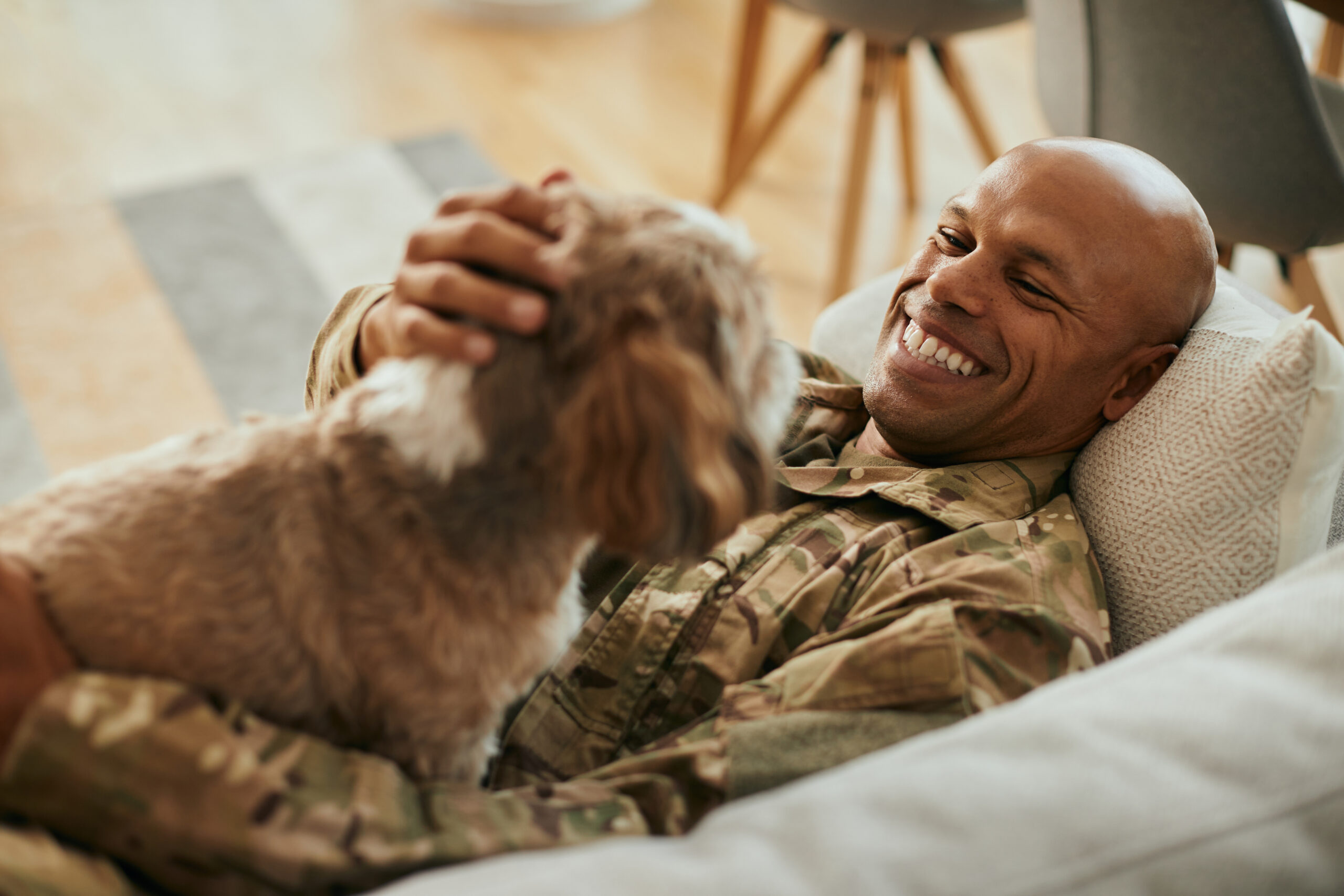 Happy African American military man enjoys with his dog at home.